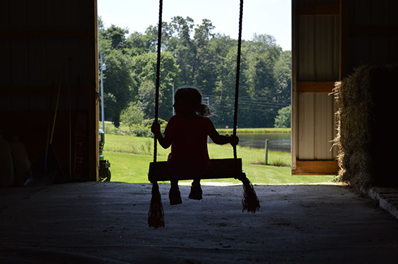 A little girl swings in a barn.