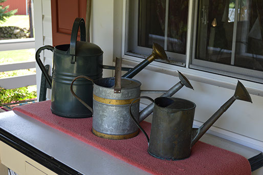 Antique watering cans decorate a table on the porch of the rental lodge.
